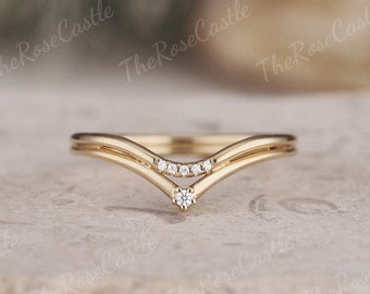 May include: A gold-colored ring with a V-shaped design. The ring features small, clear gemstones set in the center and at the bottom of the V. The words "The Rose Castle" are repeated in the background.