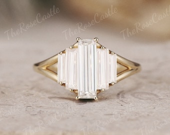 May include: A gold engagement ring with a large, rectangular emerald-cut diamond center stone and smaller baguette-cut diamonds on either side.