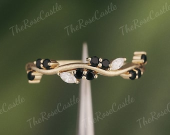 Op de afbeelding: Een delicate gouden ring met een golvend ontwerp met zwarte en witte marquise-vormige edelstenen. De ring is bezet met kleine zwarte edelstenen langs de band.