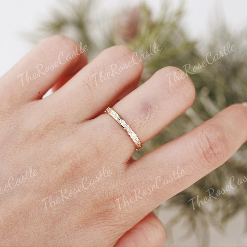 K&ouml;nnte beinhalten: Ein goldfarbener Ring mit kleinen, klaren Steinen auf der Oberseite. Der Ring befindet sich an einem Finger, und der Hintergrund ist unscharf. Der Ring scheint ein Ehering oder ein zarter Modeschmuckring zu sein.