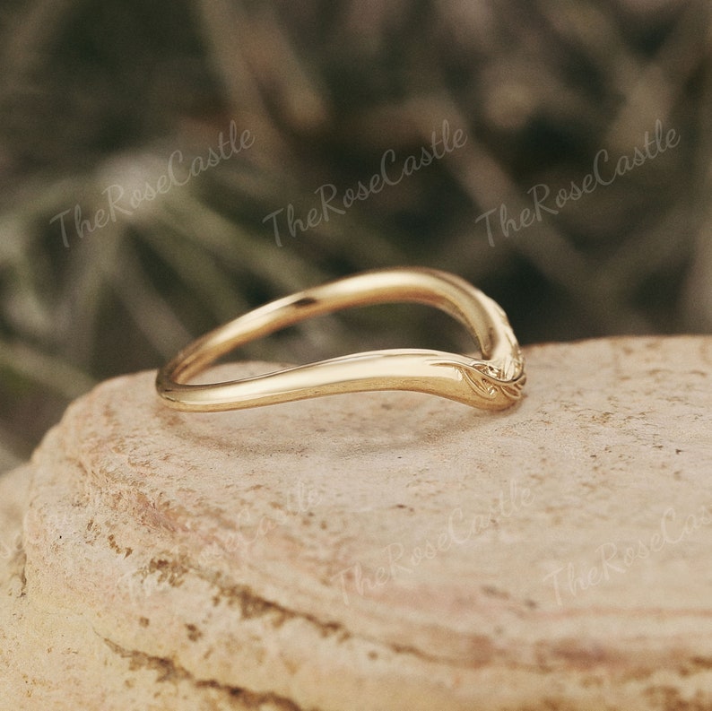 May include: A delicate gold band ring with a curved design and a floral detail on the side.