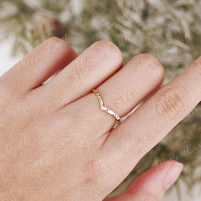 May include: A gold band ring with a V-shaped design and small clear stones set in the band.