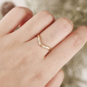 May include: A gold-colored ring with a V-shaped design and floral details. The ring is worn on a finger.