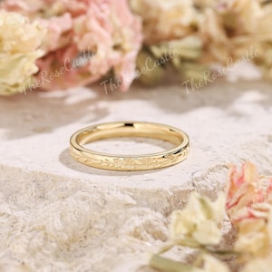 K&ouml;nnte beinhalten: Ein goldfarbener Ring mit floralem Muster. Der Ring ist vor einem neutralen Hintergrund mit zarten rosa und wei&szlig;en Blumen platziert. Das Design des Rings zeigt zarte Bl&auml;tter und Bl&uuml;ten.