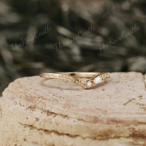 May include: A delicate gold band with a v-shaped design and a small diamond set in the center. The band is adorned with a floral pattern.