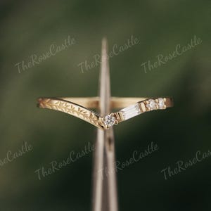 May include: A delicate gold ring with a V-shaped band adorned with small diamonds and a leaf design.