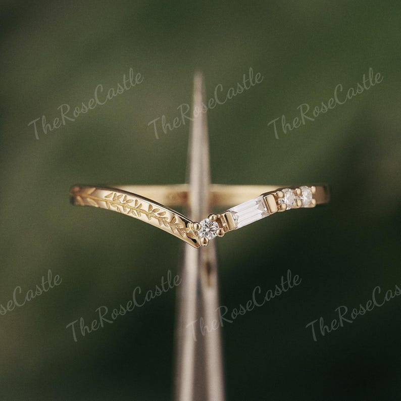 May include: A delicate gold ring with a V-shaped band adorned with small diamonds and a leaf design.