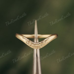 May include: A gold-toned ring with a delicate, curved design featuring a stylized floral motif. The ring is shown on a silver-toned tool.