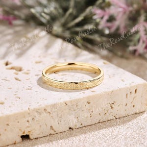K&ouml;nnte beinhalten: Ein goldfarbener Ring mit floralem Muster. Der Ring liegt auf einer hellen, strukturierten Oberfl&auml;che. Das Design des Rings zeigt zarte Bl&auml;tter und Bl&uuml;ten, die eine elegante und zeitlose &Auml;sthetik schaffen. Der Ring ist ein Symbol f&uuml;r Engagement und Liebe.