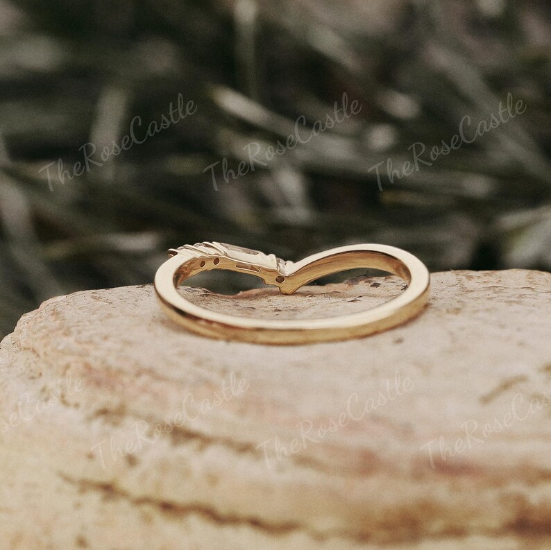 May include: A gold band ring with a single, prong-set, rectangular-shaped gemstone. The ring is set on a rock.