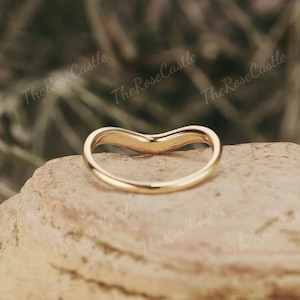 May include: A gold-colored, curved wedding band ring. The ring is made of a smooth, shiny metal and is designed to fit snugly on a finger.