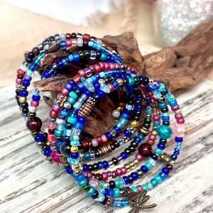 May include: A stack of colorful beaded bracelets with a dragonfly charm. The bracelets are made with various shades of blue, turquoise, red, and gold beads.