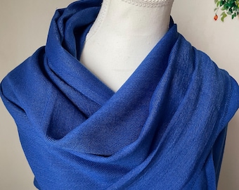May include: A vibrant blue scarf draped over a white mannequin. The scarf is made of a soft, woven fabric and is wrapped around the mannequin's neck and shoulders. The scarf's color is a rich, saturated blue, and it appears to be lightweight and flowing.