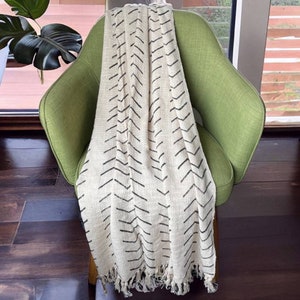 May include: A white throw blanket with black chevron pattern and fringe trim. The blanket is draped over a green armchair.