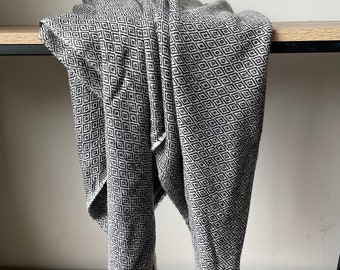 Peut inclure: Une couverture en tissu gris et noir à motif losange. La couverture est pliée et posée sur une étagère en bois.