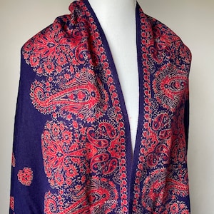 Può includere: Uno scialle blu navy con un motivo paisley rosso e crema. Lo scialle è drappeggiato su un manichino bianco.