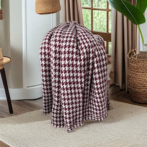 Könnte beinhalten: Eine burgunderrote und weiße, gefaltete Wolldecke mit Hahnentrittmuster auf einem hellbraunen Teppich.