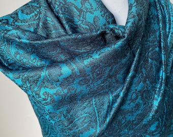 May include: A teal blue paisley patterned scarf with a black background. The scarf is draped over a white mannequin.