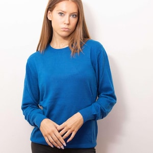 Könnte beinhalten: Ein leuchtend blauer Rundhals-Pullover. Das langärmlige Oberteil wird mit einer schwarzen Hose kombiniert. Das Model steht vor einem weißen Hintergrund. Der Pullover ist aus einem weichen Material.