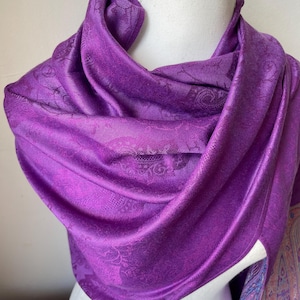 Peut inclure: Un châle en pashmina violet à motif paisley. Le châle est drapé sur un mannequin blanc.
