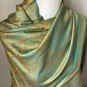Peut inclure: Un châle à motifs bleu sarcelle et or avec un motif paisley. Le châle est drapé sur un mannequin blanc.