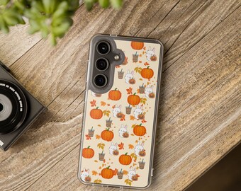 May include: A clear phone case featuring a repeating pattern of orange pumpkins, white bunnies, coffee cups, and autumn leaves on a beige background. The case is on a wooden surface.