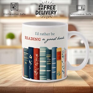 May include: White ceramic mug featuring a black and red design of stacked books. The mug has the text "I'd rather be reading a good book" printed on it.