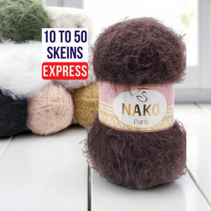 Puede incluir: Primer plano de un ovillo de lana Nako Paris marrón oscuro, con una etiqueta rosa y dorada. Otros ovillos de lana de varios colores se ven en el fondo. El texto en la imagen dice "10 a 50 madejas express."