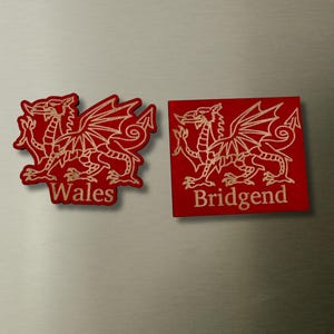May include: Two red magnets featuring a gold-coloured Welsh dragon design. The left magnet is die-cut in the shape of the dragon with the text Wales below it. The right magnet is rectangular with the same dragon design and the text Bridgend below it.