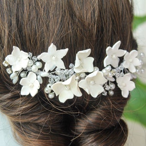 in this photograph the white porcelain flower hair piece is seen being placed on the head of the brown haired bride