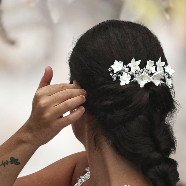 in this photograph the white porcelain flower hair piece is seen being placed on the head of the brown haired bride