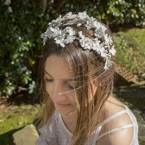 In this image we can see the bride with her handmade white porcelain flower and leaf tiara more closely in profile looking slightly down into a garden.