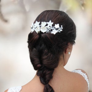 in this photograph the white porcelain flower hair piece is seen being placed on the head of the brown haired bride in silver wire