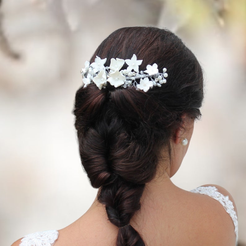 in this photograph the white porcelain flower hair piece is seen being placed on the head of the brown haired bride in silver wire