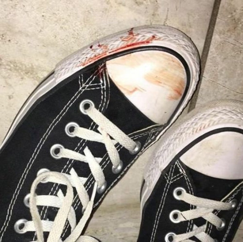 May include: A pair of black canvas sneakers with white laces and a white rubber sole. The sneakers have blood stains on the toe and side of the shoe.