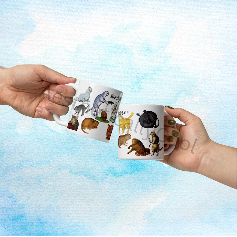 May include: Two white ceramic mugs with illustrations of various cats, including a gray cat with a sword and a black cat with a teapot. The mugs have the text "Weird Cats" on them. The mugs are held up in a toast.
