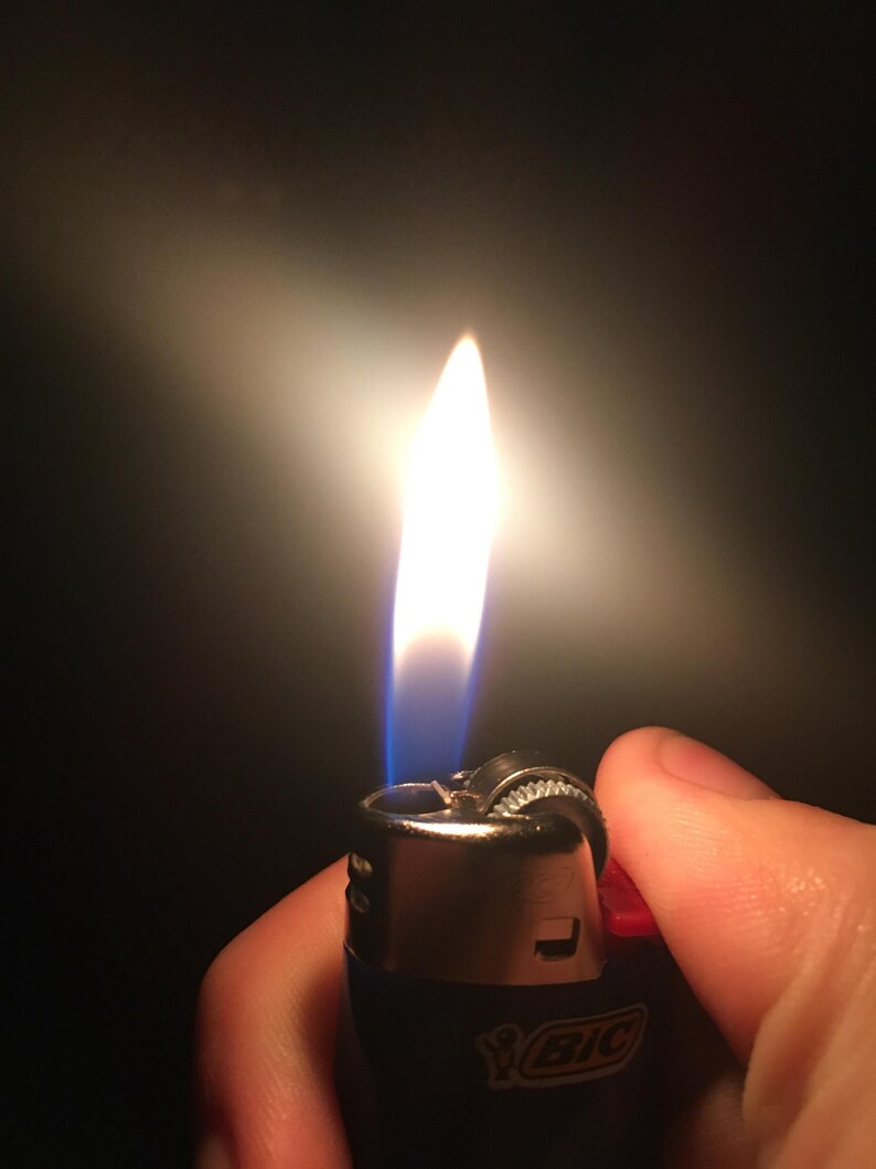 May include: A blue and silver lighter with a red top is lit, showing a bright orange flame. The lighter has the word "BIC" printed on the side.