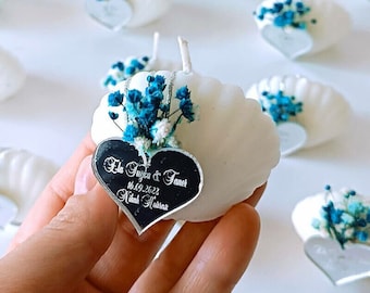 May include: White seashell shaped candle with a small bouquet of blue and white flowers and a heart-shaped mirror with the text "Ela Tuyca & Taner 18.09.2022 Nikah Merasimi" engraved on it.