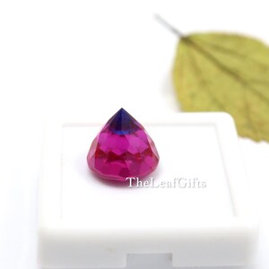 May include: A multi-faceted gemstone, displaying a colour gradient from deep blue to magenta. The gem is set in a white square, with the text "TheLeafGifts" visible. The gem is a striking piece.