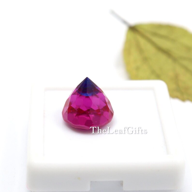 May include: A multi-faceted gemstone, displaying a colour gradient from deep blue to magenta. The gem is set in a white square, with the text "TheLeafGifts" visible. The gem is a striking piece.