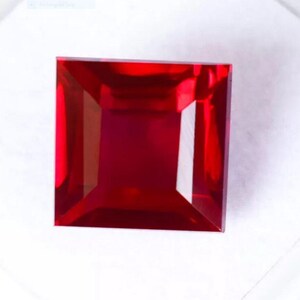 May include: A deep red square-shaped gemstone with a faceted cut.
