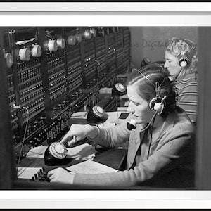 Puede incluir: Dos mujeres con auriculares trabajan en una centralita telefónica antigua. La mujer en primer plano está usando un teléfono de disco. La centralita tiene filas de botones y luces.