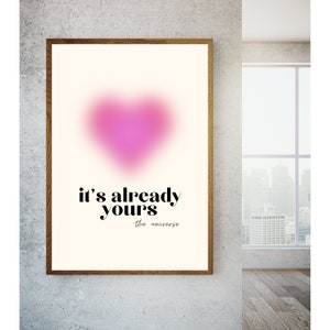 May include: A beige poster with a pink heart shape in the center and the text "it's already yours - the universe" in black.