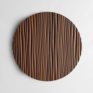 Op de afbeelding: Een ronde houten wanddecoratie met een golvend, gestreept patroon in tinten bruin en zwart.