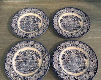 May include: Set of four blue and white ceramic plates with a floral border and a central image of a house with trees.