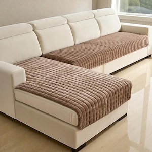 Puede incluir: Un sofá seccional con estructura color crema y fundas de asiento acolchadas marrones. Las fundas de los asientos tienen un patrón texturizado en forma de cuadrícula. El sofá está en una habitación bien iluminada, con una ventana visible al fondo.