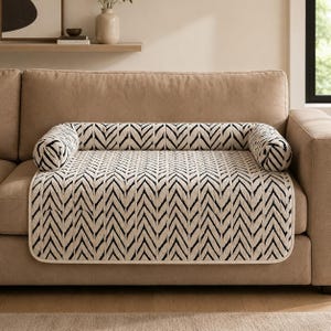 May include: A rectangular sofa cover featuring a black and white chevron pattern with a matching cylindrical bolster pillow attached to the back edge. The cover has rounded corners and a light-colored trim along the entire outer perimeter.