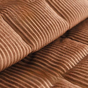 May include: Close-up of a section of brown corduroy fabric. The fabric has a ribbed texture with vertical lines and a soft, plush appearance. The color is a warm, earthy brown.