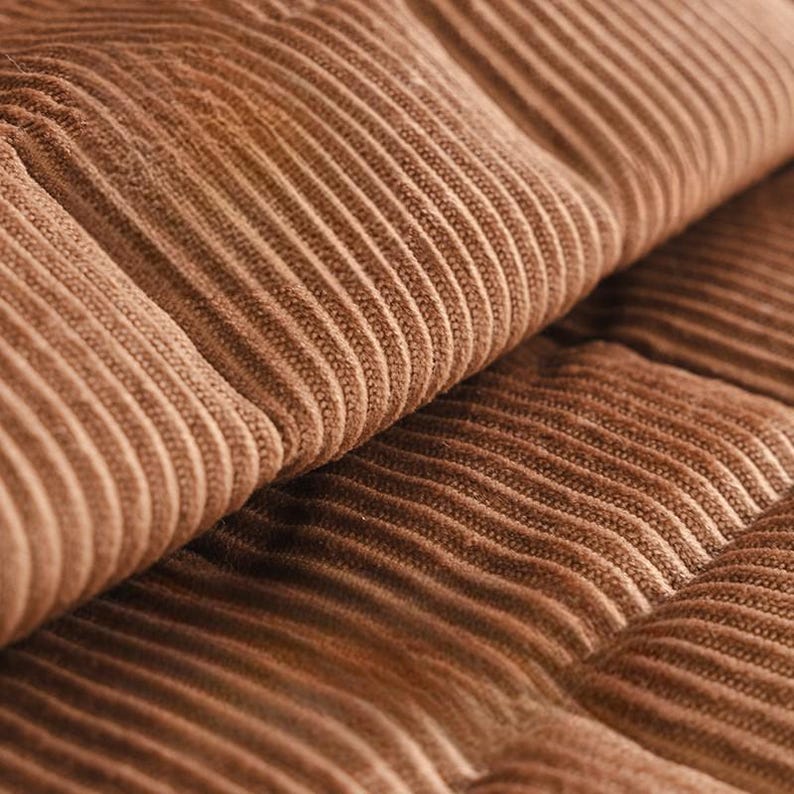 May include: Close-up of a section of brown corduroy fabric. The fabric has a ribbed texture with vertical lines and a soft, plush appearance. The color is a warm, earthy brown.