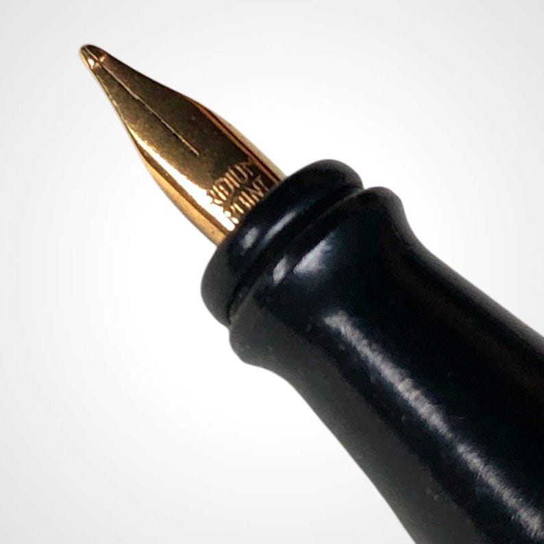 May include: Close-up of a fountain pen with a gold nib and a black barrel. The nib has the words "IRIDIUM POINT" engraved on it. The pen is set against a white background.